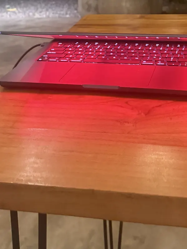 A MacBook on a wooden table at night with its screen dimmed and warmed by Sundown