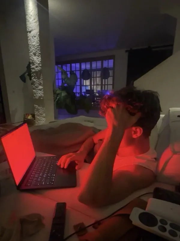 A man on a couch at night, typing on a laptop with a red Sundown screen