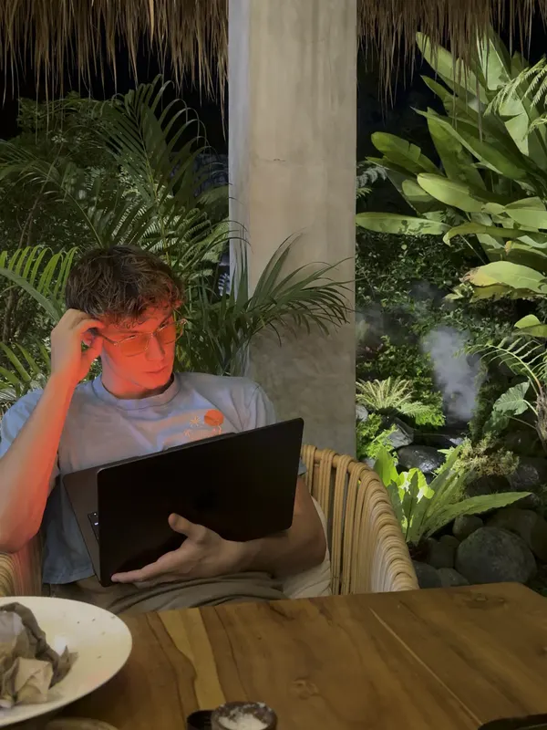 Jack Richards working on a laptop at an outdoor table at night among tropical plants