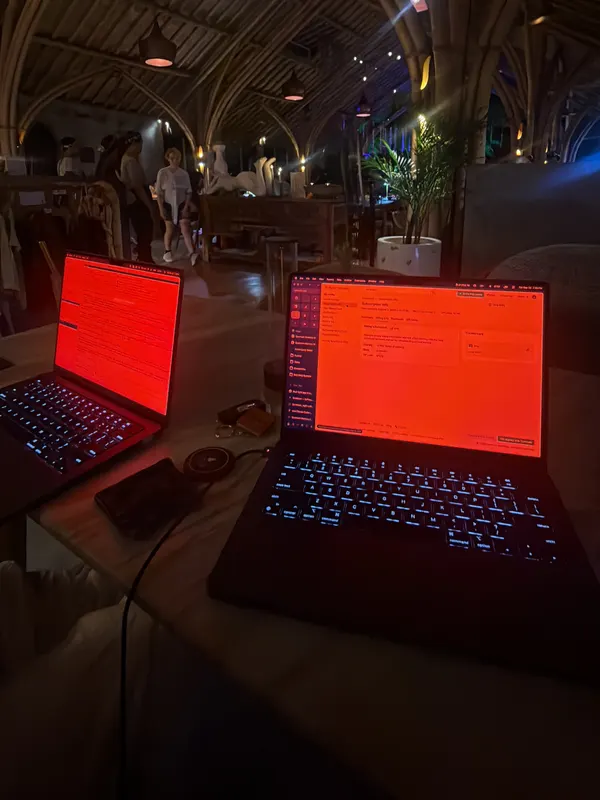 Two laptops with red Sundown screens on a table in a dim bamboo venue at night
